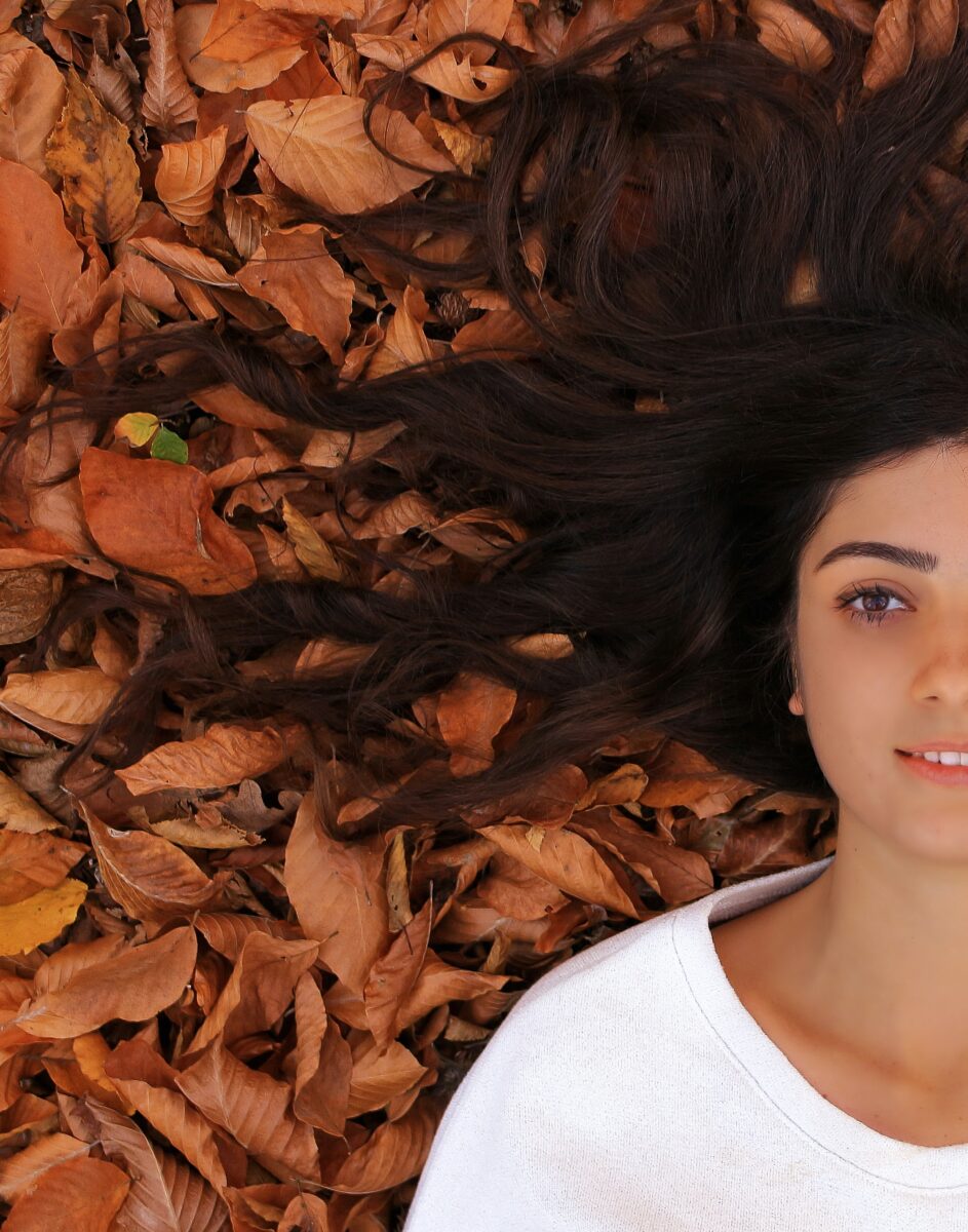 An image of a woman with long hair posing in leaves.